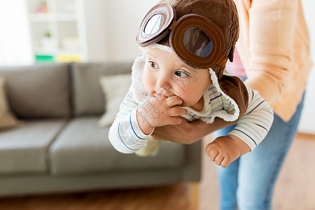 家庭,孩子母亲的快乐微笑的轻母亲家里戴着领航帽的小婴儿玩耍快乐的母亲带着婴儿家里戴着飞行员帽子图片