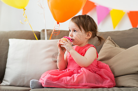 生日气球童,人庆祝快乐的女婴家里的生日聚会上吃纸杯蛋糕生日派上快乐的女婴吃纸杯蛋糕背景
