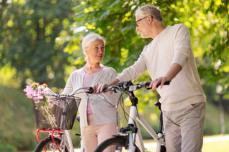 老人,人生活方式的快乐的老夫妇步行与固定自行车夏季城市公园交谈快乐的老夫妇夏季公园骑自行车图片