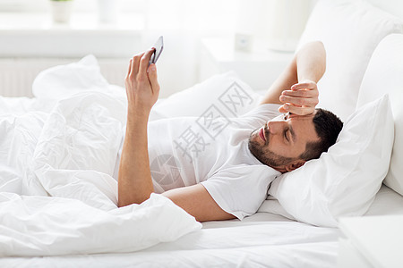 技术,互联网,通信人的快乐的轻人智能手机上发短信家里早上床上智能手机的轻人图片