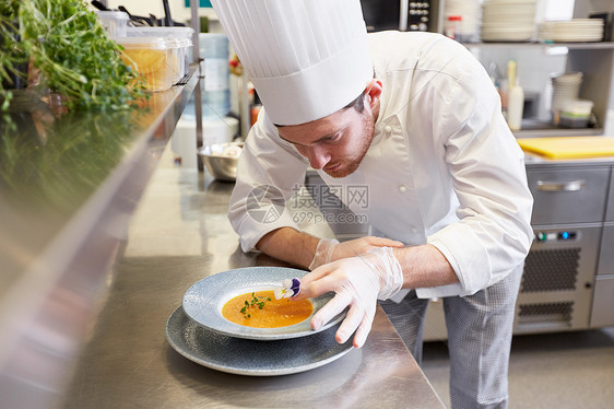 食物烹饪,职业人的快乐的男厨师烹饪服务装饰盘子的汤与花餐厅厨房快乐的男厨师餐厅厨房烹饪食物图片