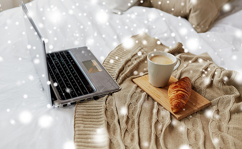 舒适的家庭,室内冬季舒适的卧室与笔记本电脑,咖啡杯牛角包床上的雪笔记本电脑,咖啡牛角包床上舒适的家图片
