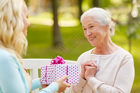 家庭,假期人的快乐的微笑的轻女儿送礼物给她的老母亲坐公园的长凳上女儿公园给迈的母亲送礼物图片