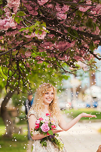 女孩樱花树下,手里着花,享受着花朵樱花盛开下的微笑女孩图片