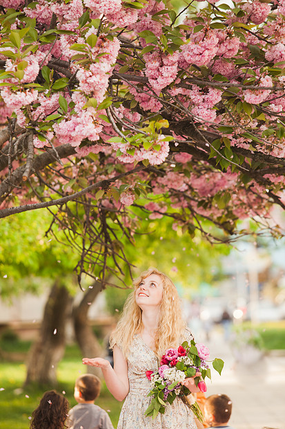 女孩樱花树下,手里着花,享受着花朵樱花盛开下的微笑女孩图片