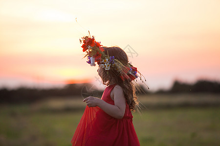 穿着红色连衣裙的美丽微笑的小女孩正,头上戴着个花环田野里跳舞图片