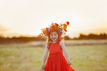 穿着红色连衣裙的美丽微笑的小女孩正,头上戴着个花环田野里跳舞图片