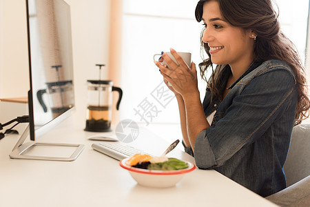 轻的女人电脑桌上吃早餐图片