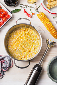 美味的素食玉米汤烹饪锅与棍子搅拌机配料白色木制背景,顶部的健康食品的图片