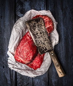 生牛肉与旧肉刀深蓝色木制背景,顶部视图图片
