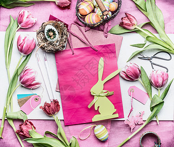 复活节文字复活节工作区粉红色郁金香花复活节装饰品,用鸡蛋,纸袋篮子,顶部视图,文字的地方背景