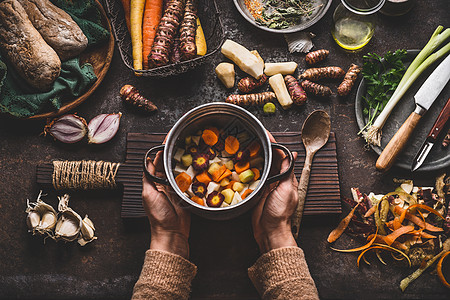 女手着平底锅,深色的乡村厨房桌子上放着五颜六色的蔬菜丁,素食烹饪原料工具健康干净的季节食品烹饪饮食理念图片