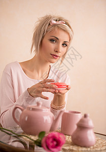 轻漂亮的金发女人喝茶的时候吃马卡龙她很满意短发粉红色现代风格图片