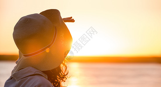 轻美丽的女人戴着顶帽子,夕阳的光线下看着远方后的照片图片