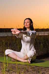 美丽的轻女人日落时坐湖边瑜伽图片