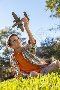 个小男孩坐外的草地上玩玩具模型飞机图片