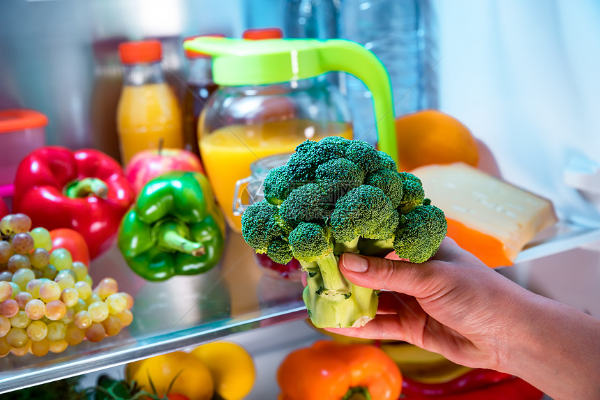 女人打开的冰箱里花椰菜健康的食物图片