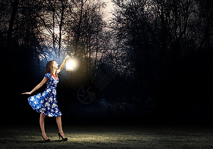 带灯笼的女人穿着蓝色连衣裙的轻女人夜间树林里散步图片