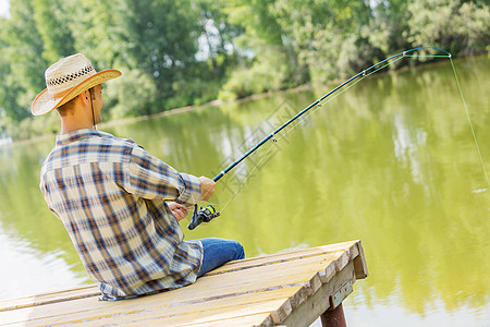 夏天钓鱼戴帽子的轻人坐桥上钓鱼图片