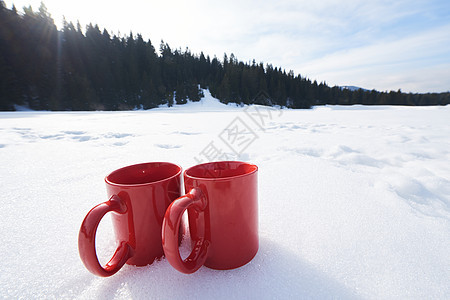 两辆红色的热茶饮料雪中,美丽的冬季阳光明媚的天,与木屋森林的背景图片