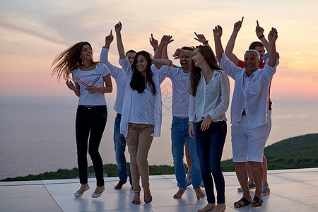 群快乐的轻人现代家庭的聚会上跳舞,玩得很开心,背景日落海洋图片