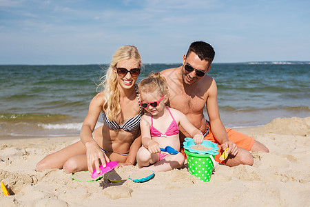 家庭,旅行,假期人的快乐的男人,女人小女孩戴着太阳镜夏天的海滩上玩沙子玩具图片