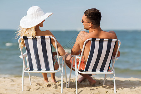 爱情,旅行,旅游,夏天人的微笑的夫妇度假穿着泳装坐椅子上,后海滩上晒太阳背景图片