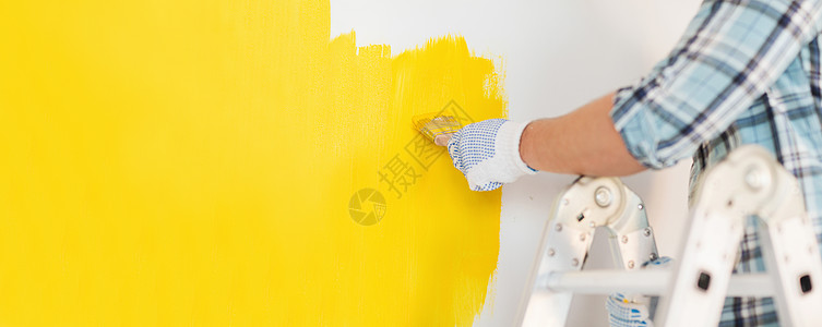 修理家庭改造的男的手手套上涂黄色油漆的墙壁把戴手套的男人关来画墙背景图片