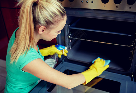 人,家务家务快乐的女人用瓶喷雾清洁剂清洁烤箱家里厨房图片