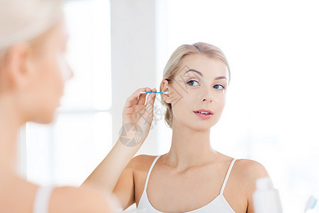 美容,卫生人的轻妇女用棉签清洁耳朵,并家里的浴室照镜子背景图片