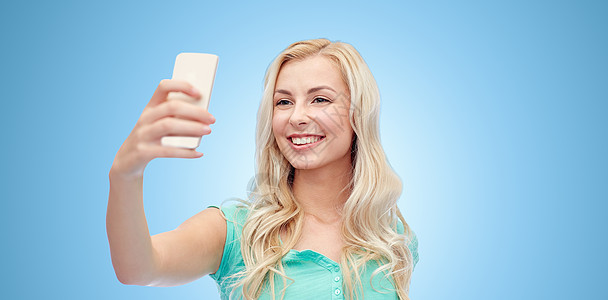 情感,表情人的快乐的微笑轻妇女十几岁的女孩自拍与智能手机蓝色背景图片