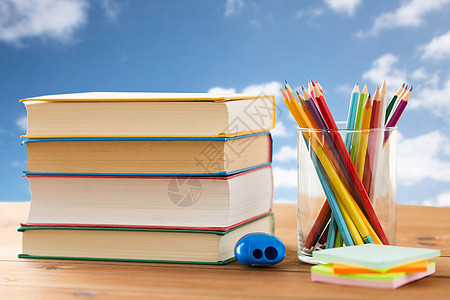 教育,学校,创造力象蜡笔彩色铅笔与书籍,贴纸锐器木制桌子上蓝天云背景图片