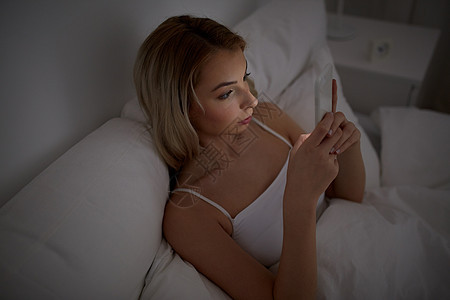 技术,互联网,沟通人的轻的女人智能手机上发短信家里的卧室晚上图片