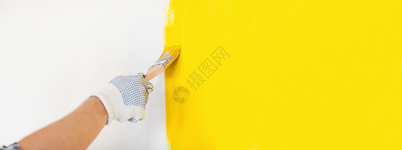 修理家庭改造的男的手手套上涂黄色油漆的墙壁把戴手套的男人关来画墙背景图片