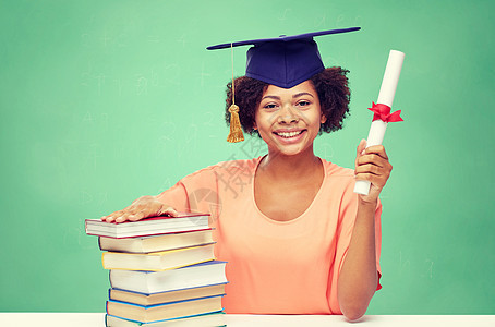 教育,学校,知识,毕业人的快乐的微笑非裔美国学生女孩学士帽与书籍文凭的绿色粉笔板背景图片