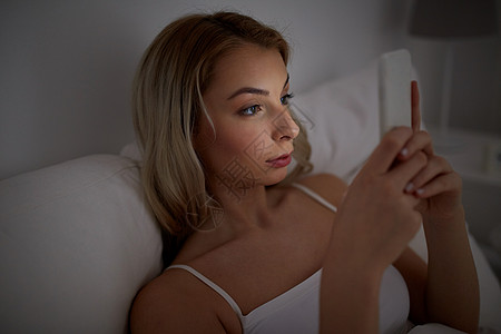 技术,互联网,沟通人的轻的女人智能手机上发短信家里的卧室晚上图片