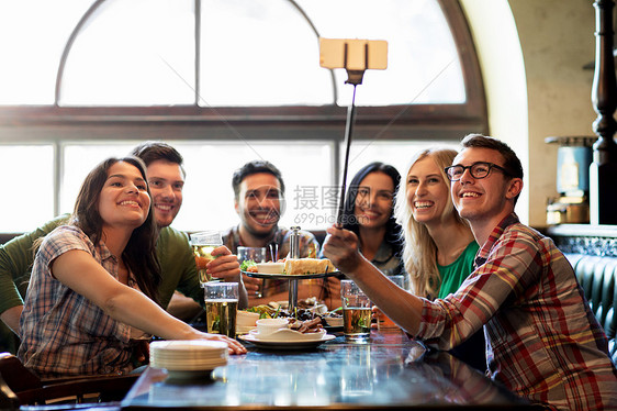 人,休闲,友谊技术快乐的朋友用智能手机自拍棒拍照,喝啤酒,酒吧酒吧吃零食图片