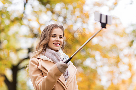 季节,技术人的美丽的轻快乐的女人秋天公园用智能手机自拍棒拍照图片