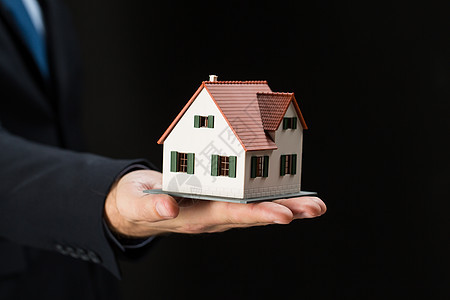 建筑建筑建筑房地产物业密切商人房地产经纪人黑色背景下手持房屋住宅模型图片