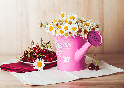 雏菊乡村的水壶里,白色的餐巾纸木制的背景上旁边盘装满樱桃的盘子背景图片