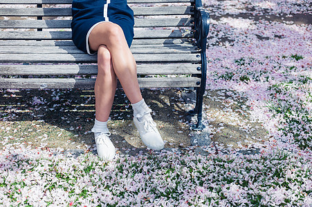 个轻女人的腿脚公园的长凳上放松,地上开着樱花图片