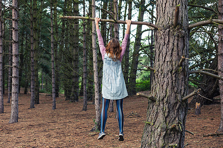 个轻的女人正森林里爬棵树,挂树枝上图片