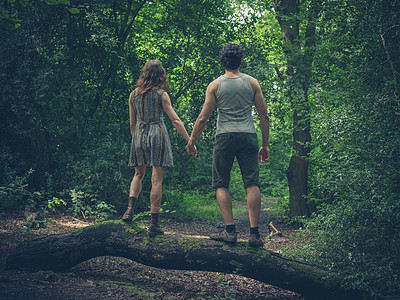 轻的夫妇牵着手,站森林里的根原木上图片