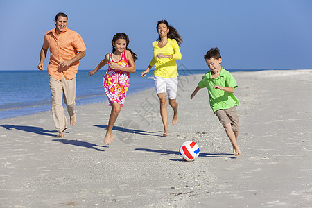 个幸福的家庭,母亲,父亲两个孩子,儿子女儿,阳光明媚的沙滩上踢足球足球背景图片