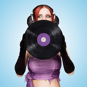 情感女孩戴着巨大的老式音乐耳机,并持紫色的LP微槽乙烯基唱片蓝色背景图片