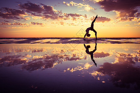 日落时海滩上练瑜伽的女人的剪影背景图片