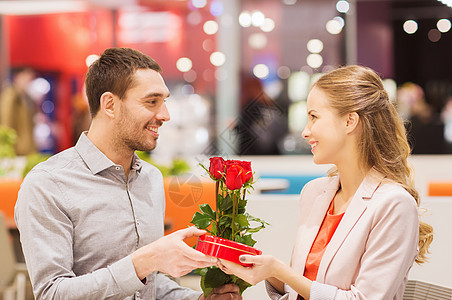 爱情,浪漫,情人节,夫妇人的快乐的轻人带着红花送礼物给微笑的女人购物中心的咖啡馆图片