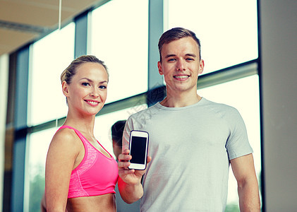 健身,运动,广告,技术饮食微笑的轻妇女私人教练与智能手机空白屏幕健身房图片