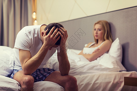 酒店,旅行,人际关系问题的心烦意乱的男人坐床上,女人坐后背景图片
