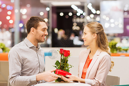 爱情,浪漫,情人节,夫妇人的快乐的轻人带着红花送礼物给微笑的女人购物中心的咖啡馆背景